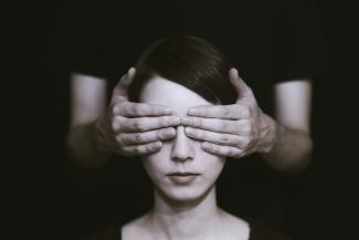 person covering the eyes of woman on dark room by Ryoji Iwata courtesy of Unsplash.