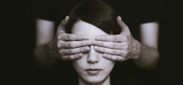 person covering the eyes of woman on dark room by Ryoji Iwata courtesy of Unsplash.